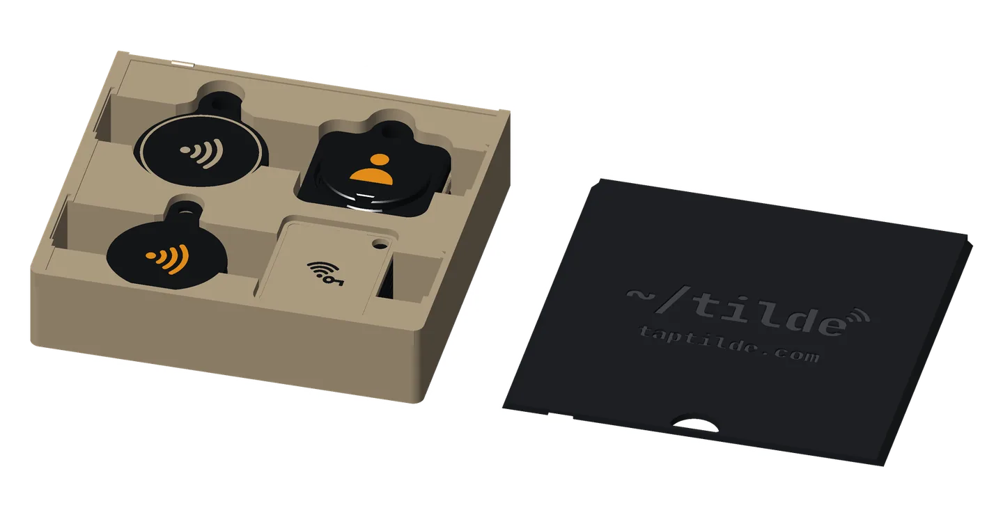 The fob storage box open, its four stacks of fobs in the three color sets, the sliding lid beside it: base coins (on top, Tap waves, orange on black), base tags (Wi-Fi password, black on khaki), premium coins (Tap waves, khaki on black) and premium tags (Person, orange on black).