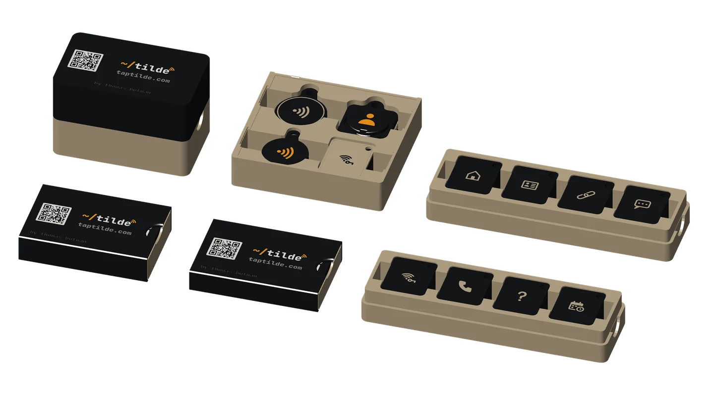 The Tilde booth table: the two giveaway boxes open with their eight stacks of base tags and the fob storage box open with its four stacks of fobs, beside the closed cards-only box and the 5- and 3-card pocket cases.